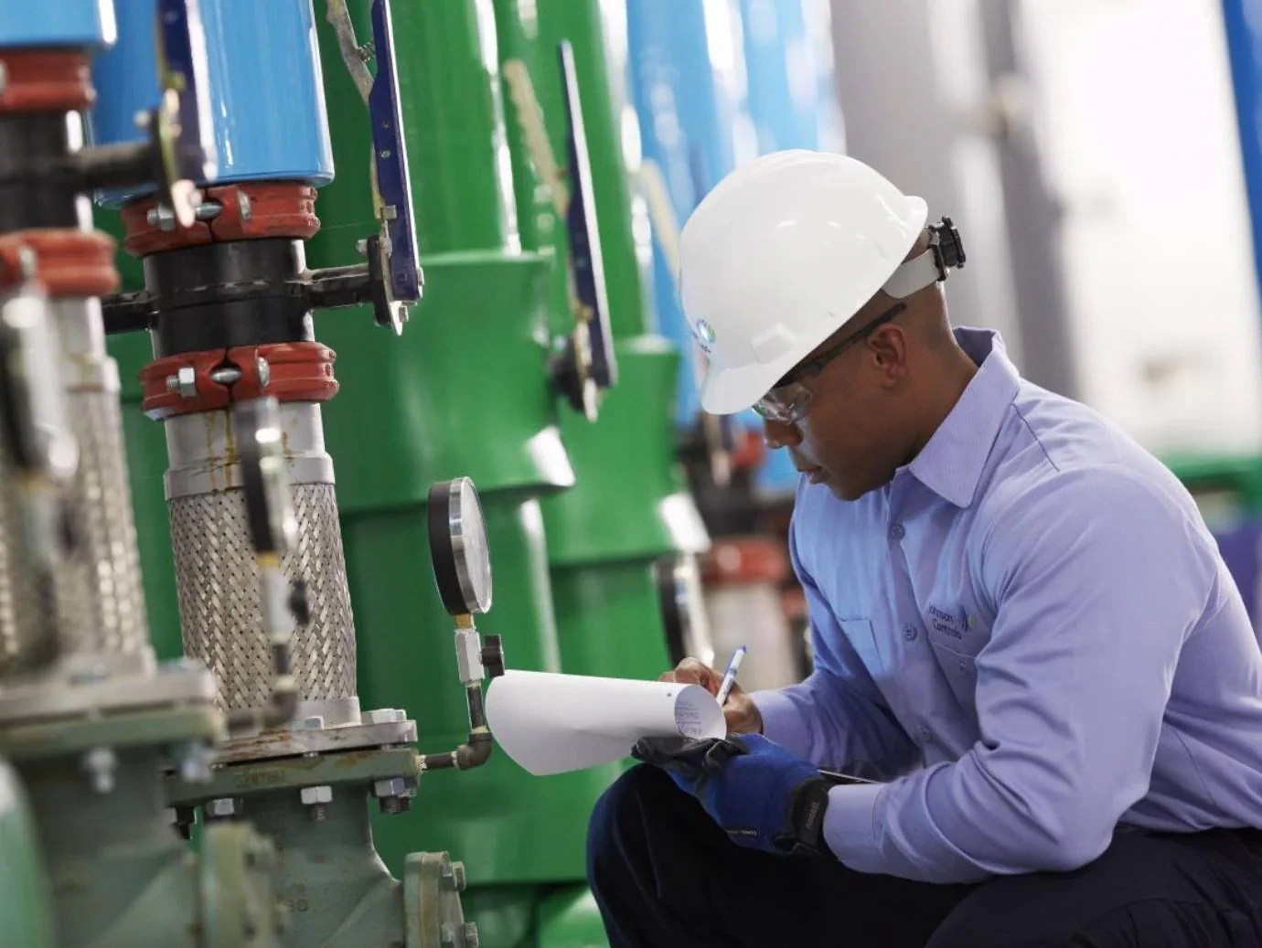 HVAC technician recording equipment readings beside mechanical piping