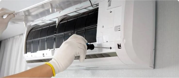 Gloved hands servicing a wall-mounted air conditioner